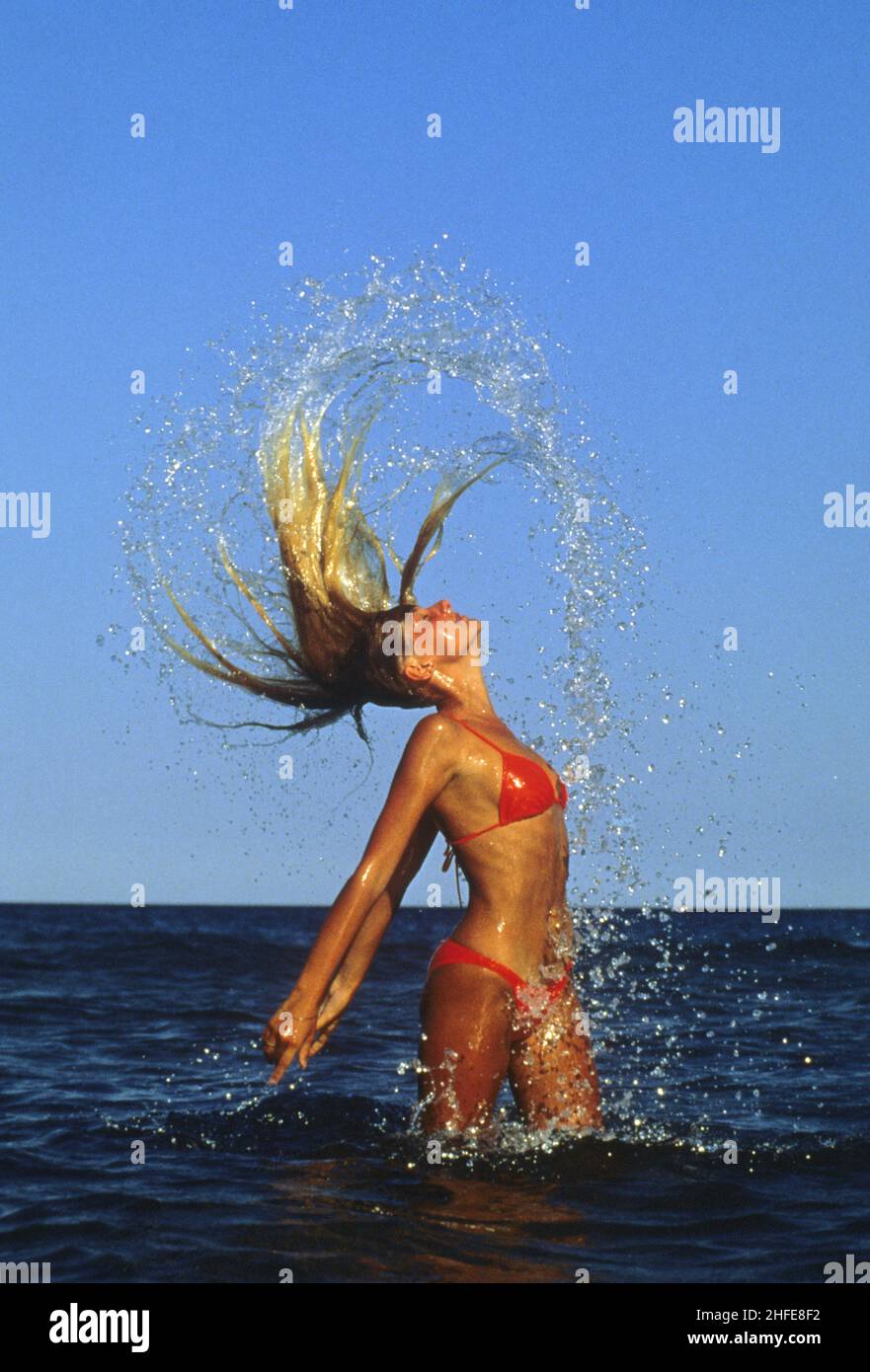 capelli biondi bella silhouette stand up profilo vista spiaggia attraverso i suoi capelli spruzzi blu cielo acqua di mare sfondo Foto Stock