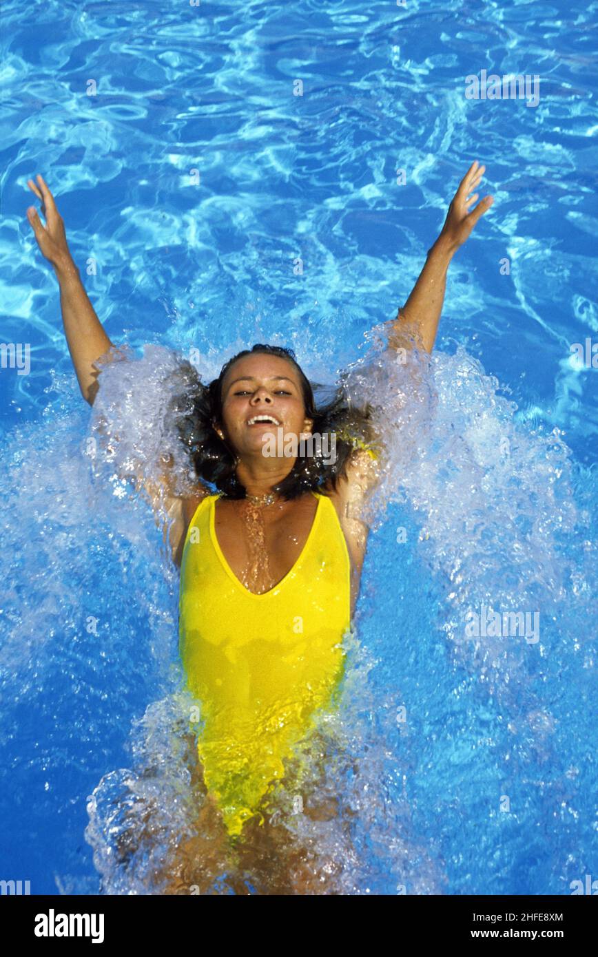 bella marrone capelli giovane donna facendo spruzzi acqua piscina guardando parte anteriore abbronzatura bellezza nuoto sulla schiena Foto Stock