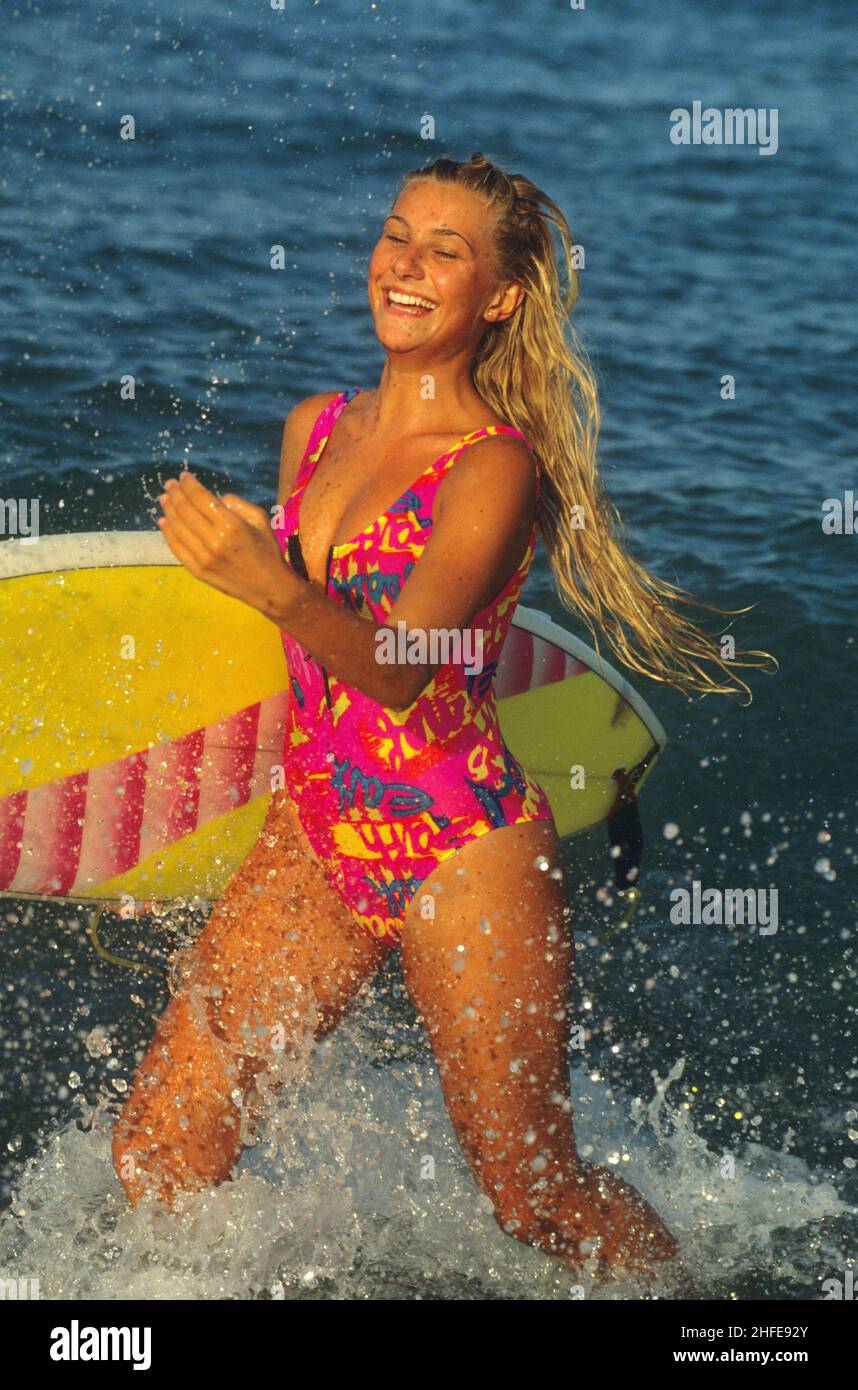 bellezza attraente capelli biondi silhouet sportivo con surf board che corre sulla spiaggia spruzza uno sfondo di acqua di mare Foto Stock