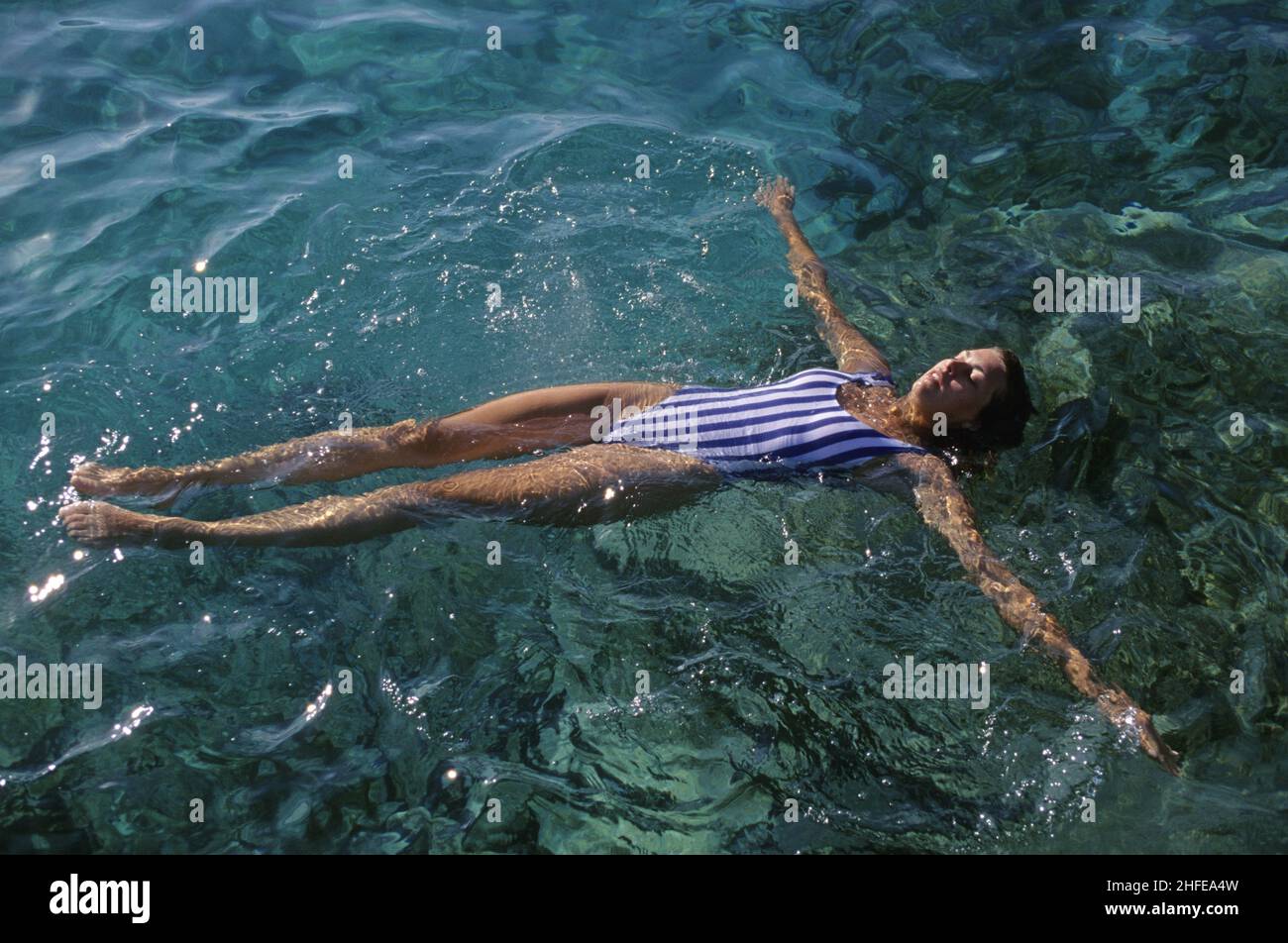 bellezza attraente dei capelli scuri prendendo il sole che nuota sulla sua schiena rilassato acqua di mare chiara intorno Foto Stock