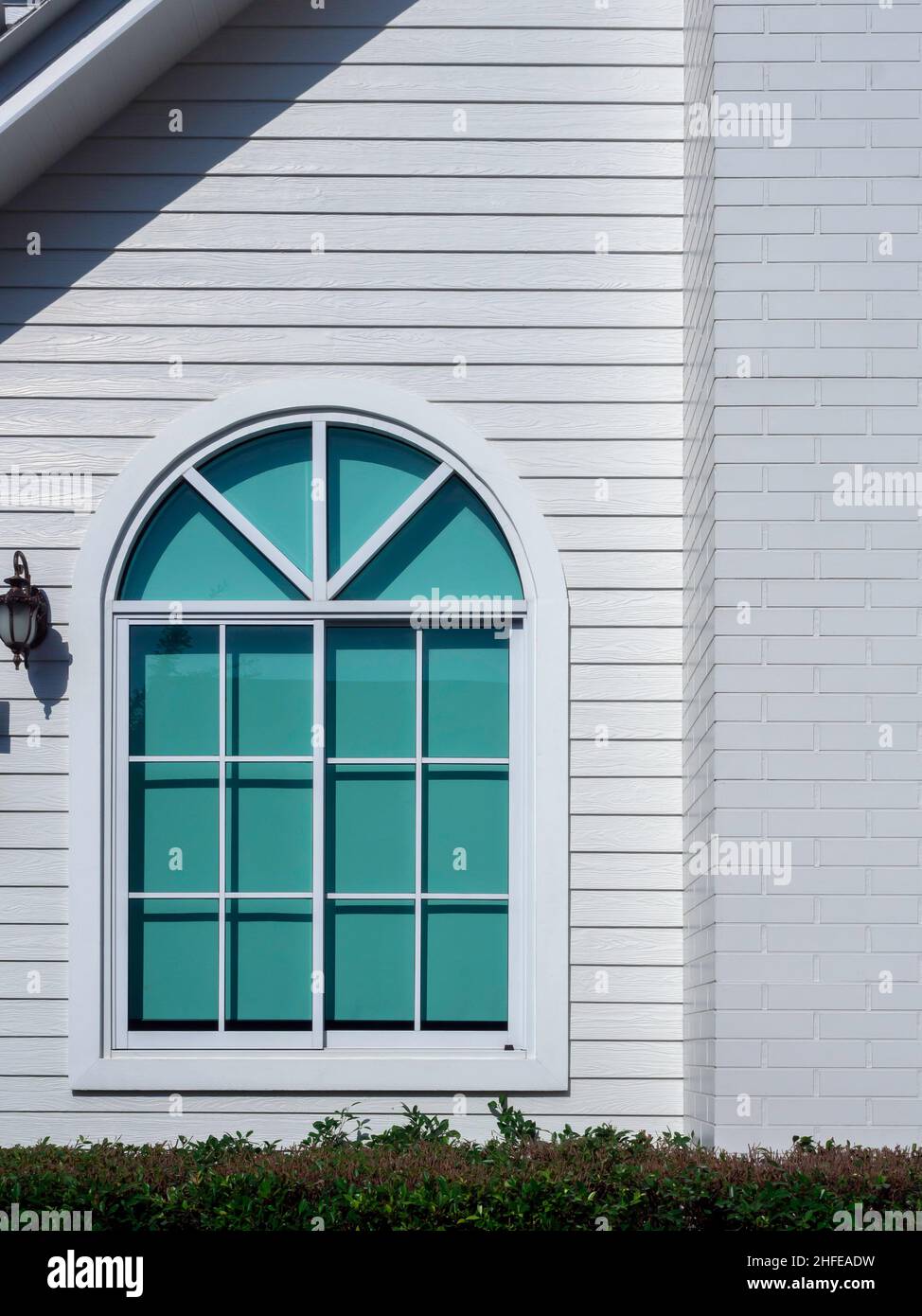 Una finestra casa bianca con vetro, telaio curvo, tenda verde decorazione sul grande residente in legno bianco, stile verticale, vista dall'esterno. Foto Stock