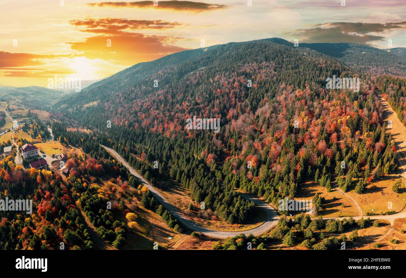 Alta vetta di montagna con foreste verdi e rosse e un colorato prato giallo sotto il cielo nuvoloso con vista panoramica del tramonto Foto Stock