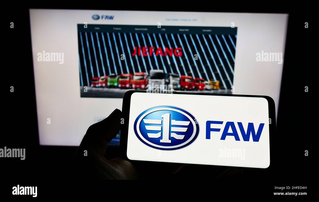 Persona che tiene il cellulare con il logo della società automobilistica cinese FAW Group Corporation sullo schermo di fronte alla pagina web. Mettere a fuoco sul display del telefono. Foto Stock