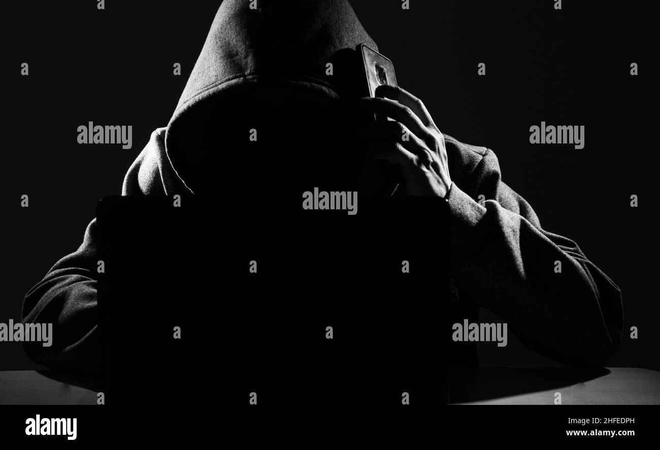 Hacker tramite smartphone. Uomini in abiti neri con volto nascosto guarda lo schermo dello smartphone Foto Stock