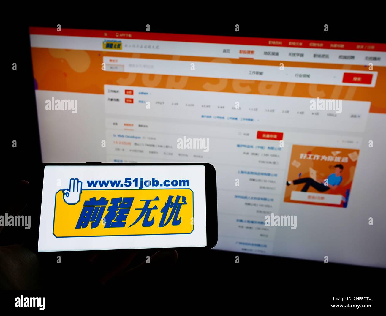 Persona che tiene il telefono cellulare con il logo della società cinese di risorse umane 51job Inc. Sullo schermo di fronte alla pagina web. Mettere a fuoco sul display del telefono. Foto Stock