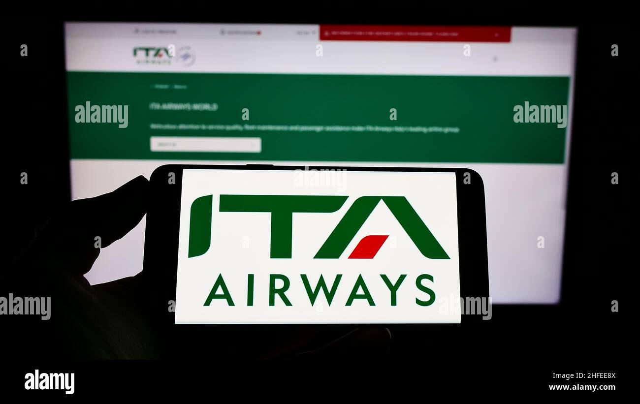Persona che detiene il cellulare con il logo della compagnia aerea Italia trasporto Aereo S.p.A. (ITA Airways) sullo schermo di fronte alla pagina web. Mettere a fuoco sul display del telefono. Foto Stock
