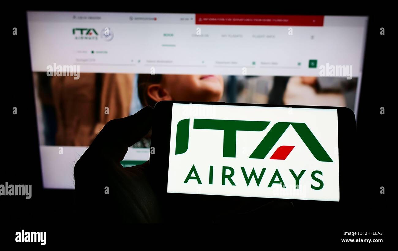 Persona che detiene il cellulare con il logo della compagnia aerea Italia trasporto Aereo Spa (ITA Airways) sullo schermo di fronte alla pagina web. Mettere a fuoco sul display del telefono. Foto Stock