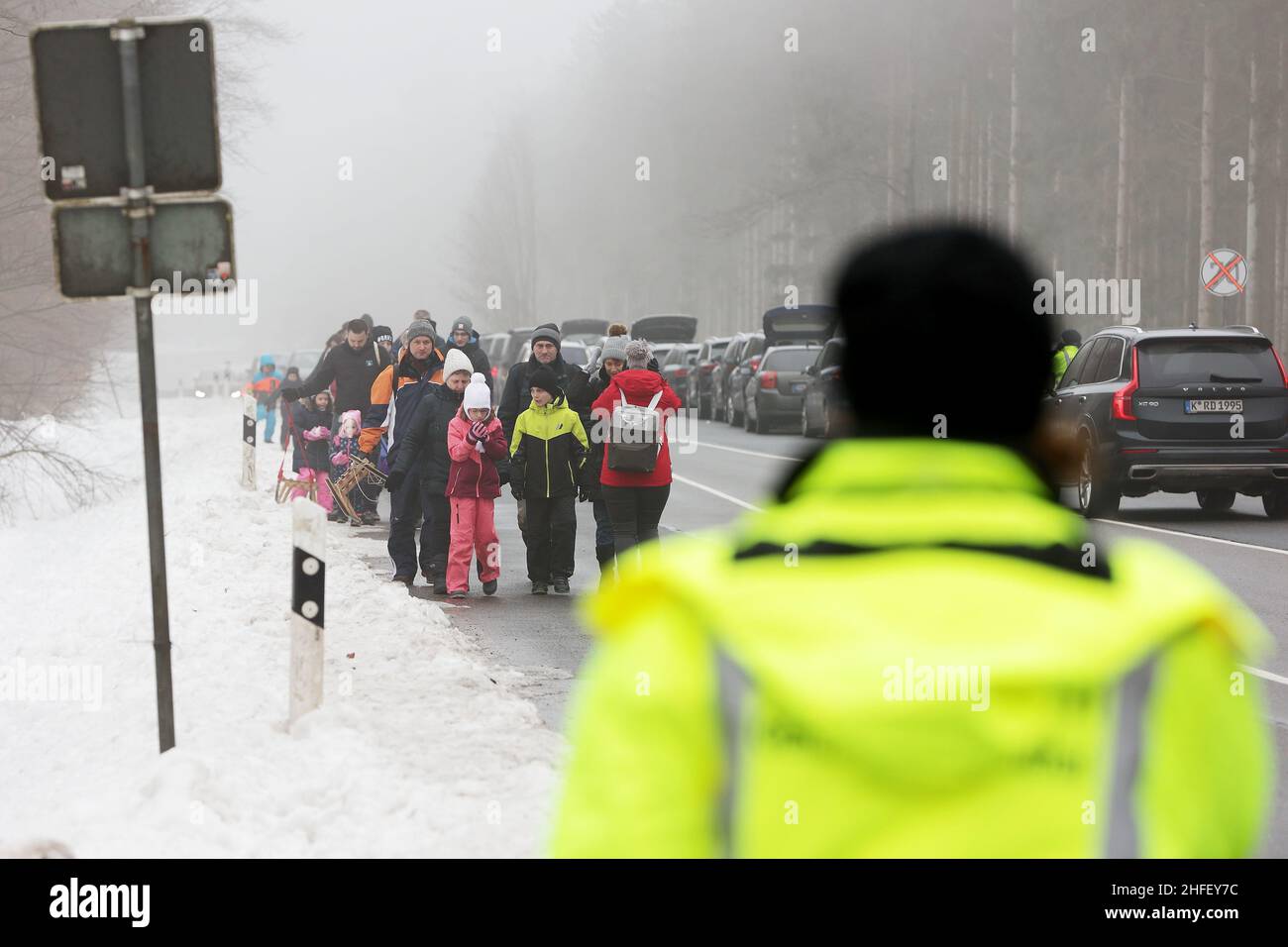 Hellenthal, Germania. 16th Jan 2022. I turisti della neve passano davanti alle auto parcheggiate sulla strada fino alle piste nella zona di sci e slittino alla 'pietra Bianca', mentre i parcheggi sono già occupati. Numerosi visitatori sono fuori e in città nella nevosa Eifel, anche se gli impianti di risalita sono chiusi. Credit: David Young/dpa/Alamy Live News Foto Stock