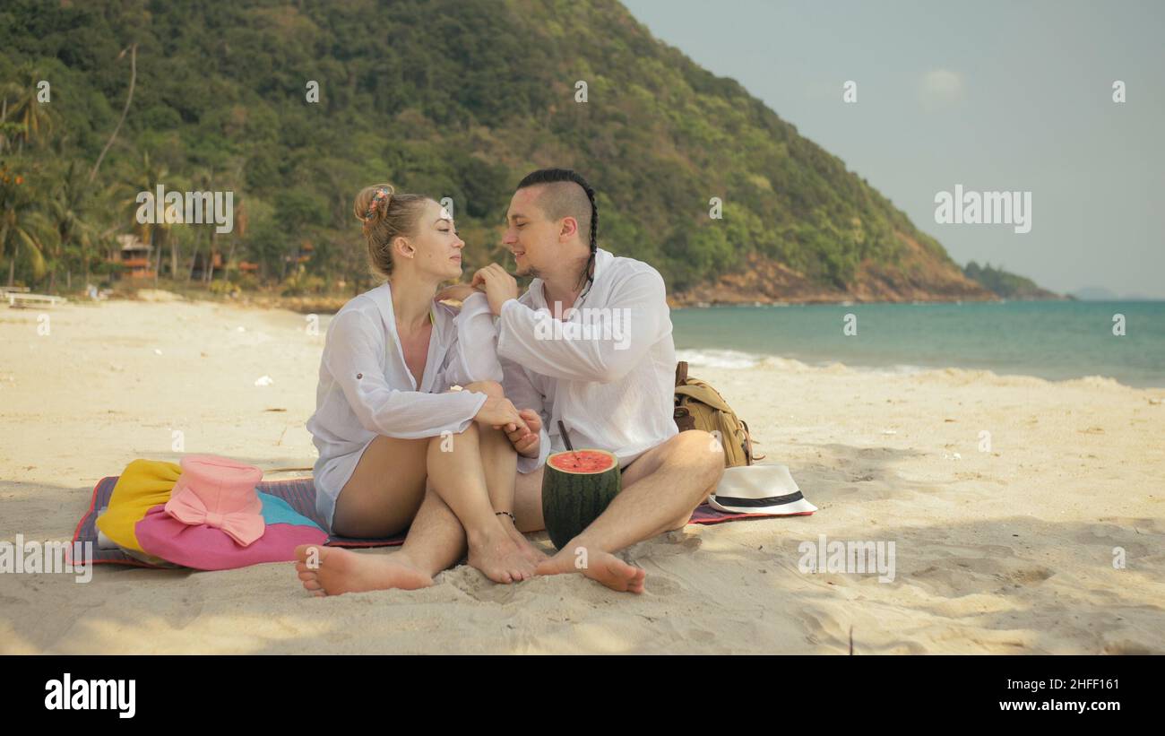 La allegra coppia d'amore che tiene e mangia fette di anguria sulla spiaggia tropicale di sabbia del mare. Amanti romantici due persone trascorrono il fine settimana estivo. Foto Stock