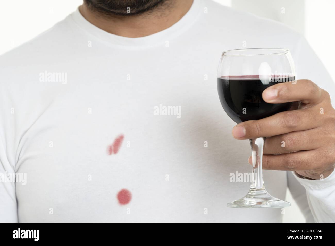 Foto ravvicinata dell'uomo che tiene il bicchiere del vino e indossa una camicia bianca colorata. Concetto di lavanderia e lavaggio abiti sporchi. Foto Stock