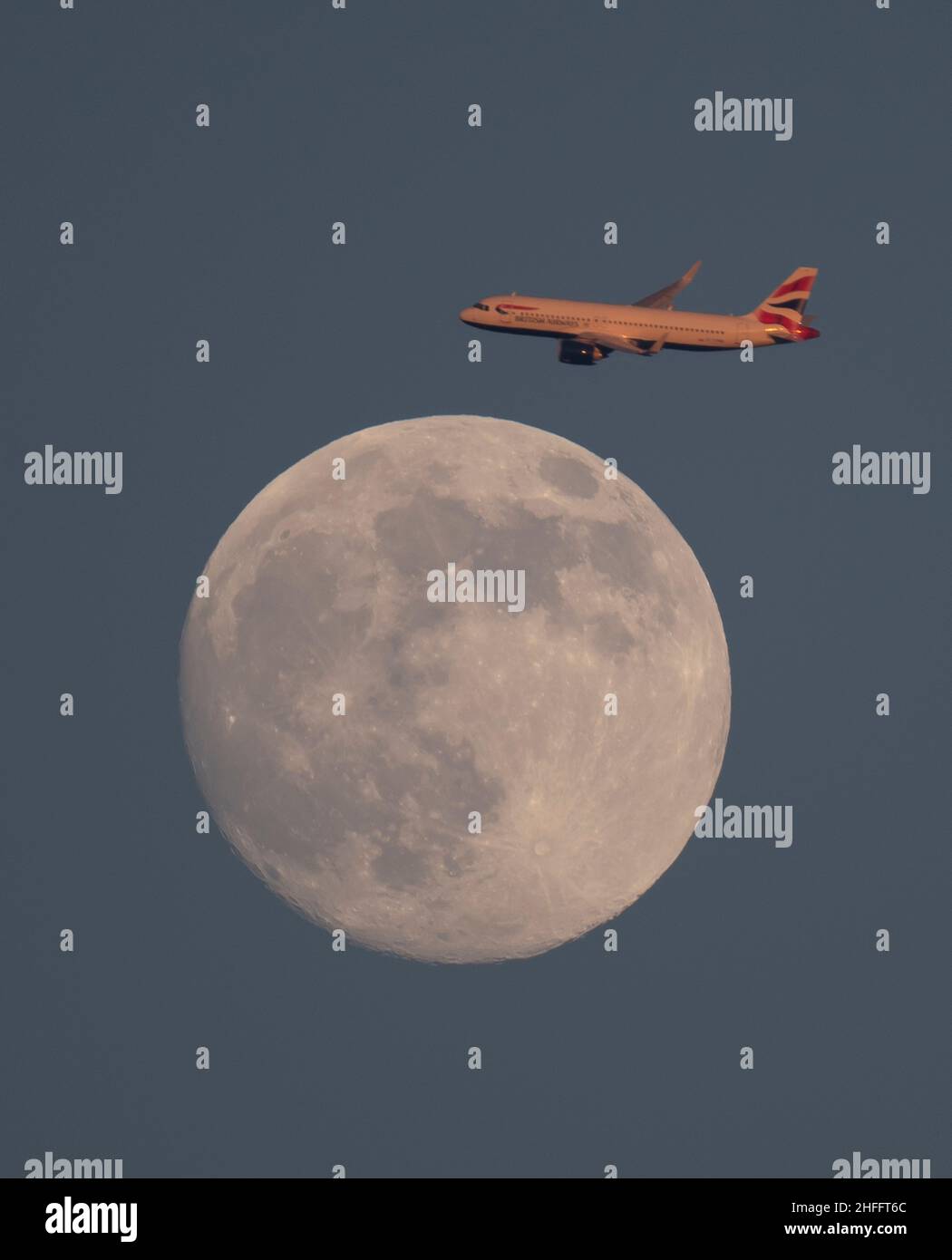 Londra, Regno Unito. 16 gennaio 2022. Volo British Airways di prima serata da Tenerife in avvicinamento a Londra Heathrow e bagnata dalla luce del sole passa la Luna quasi piena sopra Londra. Credit: Malcolm Park/Alamy Live News Foto Stock