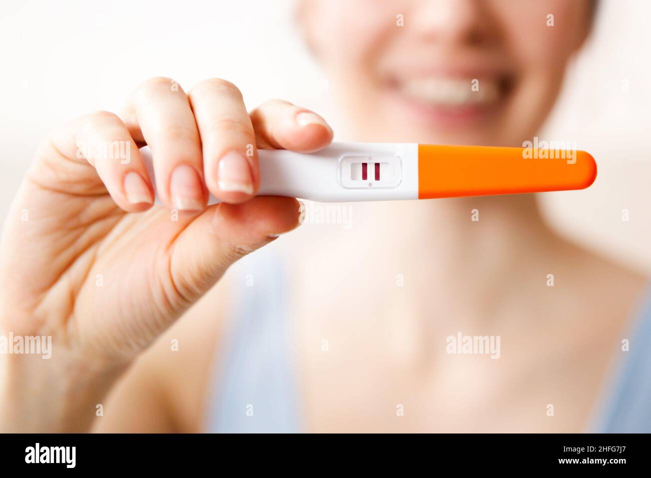 Una giovane donna felice tiene in mano un test di gravidanza positivo, il concetto di una gravidanza attesa da tempo. Foto Stock