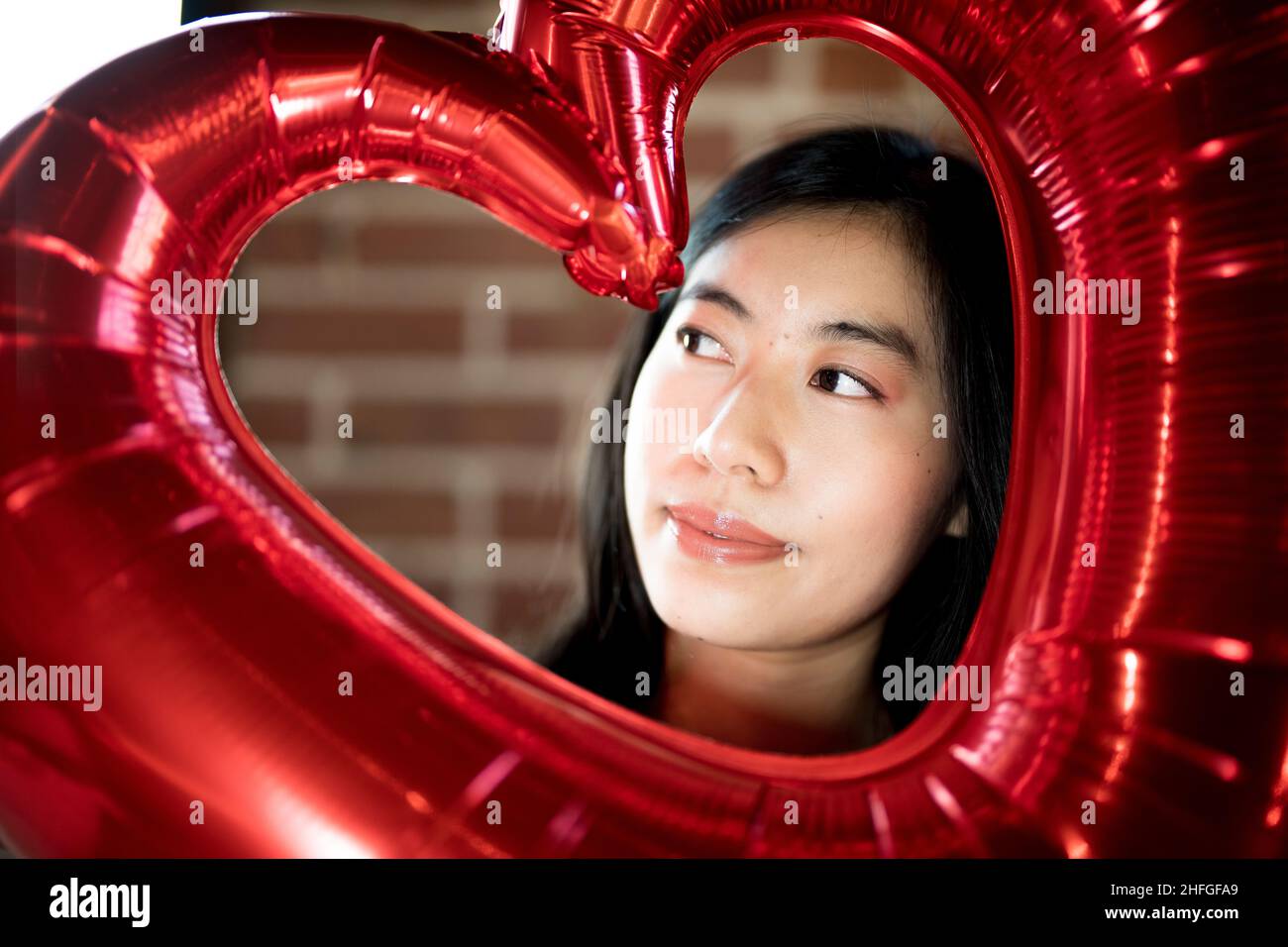 Giovane donna dell'Asia orientale che guarda attraverso la scultura di cuore di giorno di San Valentino rosso grande Foto Stock