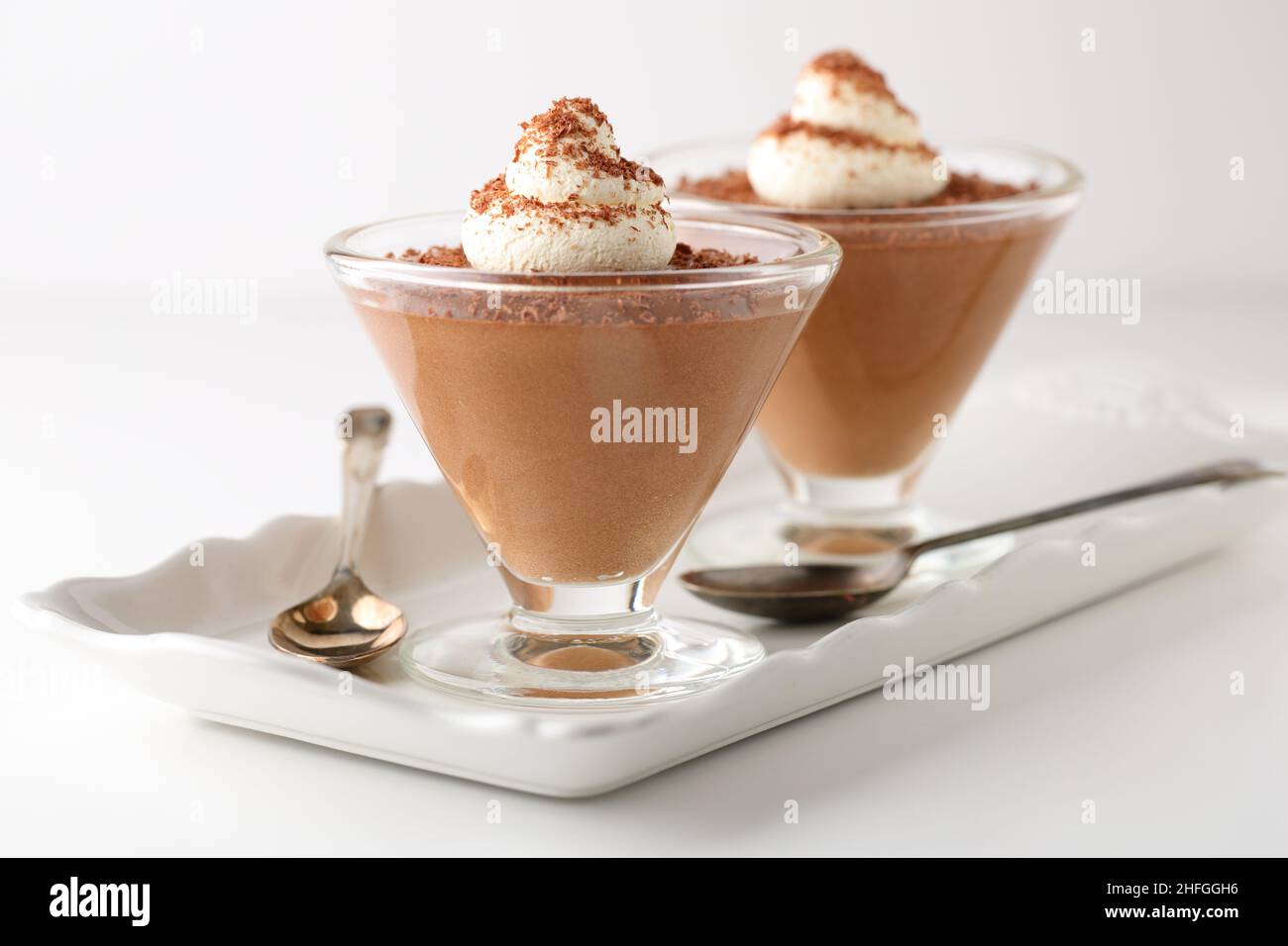 Dessert al cioccolato mousse in piatti di vetro conico su un vassoio di porcellana bianca con cucchiai, conditi con girelli di crema e cioccolato fondente grattugiato Foto Stock