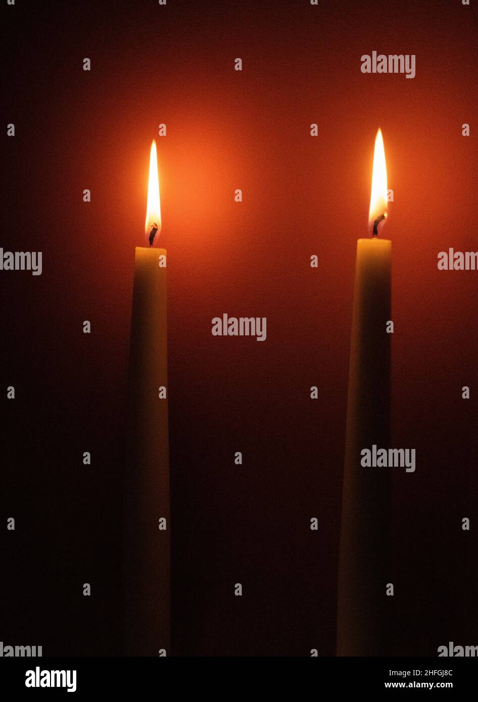 Due candele che bruciano su sfondo rosso. Foto Stock