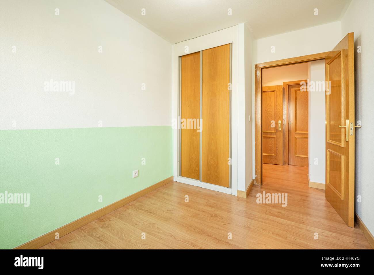 Camera con parete dipinta in due tonalità, armadio con porte scorrevoli in legno e carpenteria in rovere su pavimenti e porte. Foto Stock
