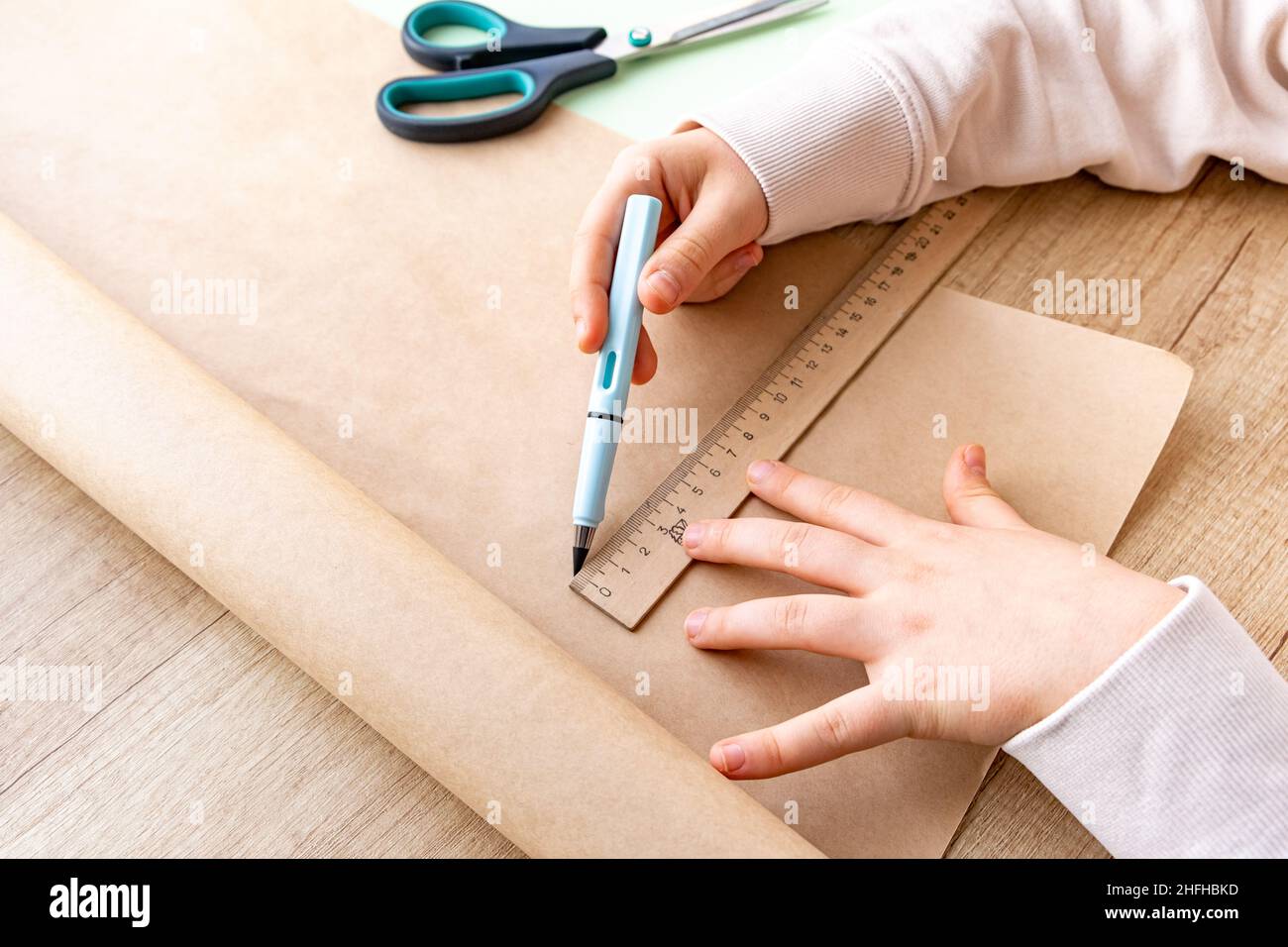 Primo piano della mano del bambino in processo di schizzo con la matita su carta artigianale. Linea retta con righello. Artigianato e imballaggio da carta ecologica. Scuola Foto Stock