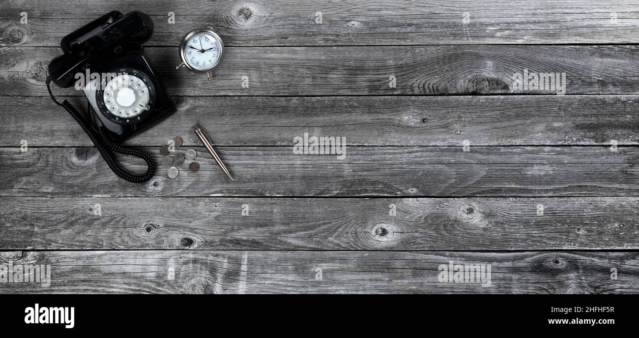 Tavolo da ufficio in legno invecchiato con telefono retrò rotante, penna, orologio e monete. Vista dall'alto con ampio spazio per le copie. Foto Stock