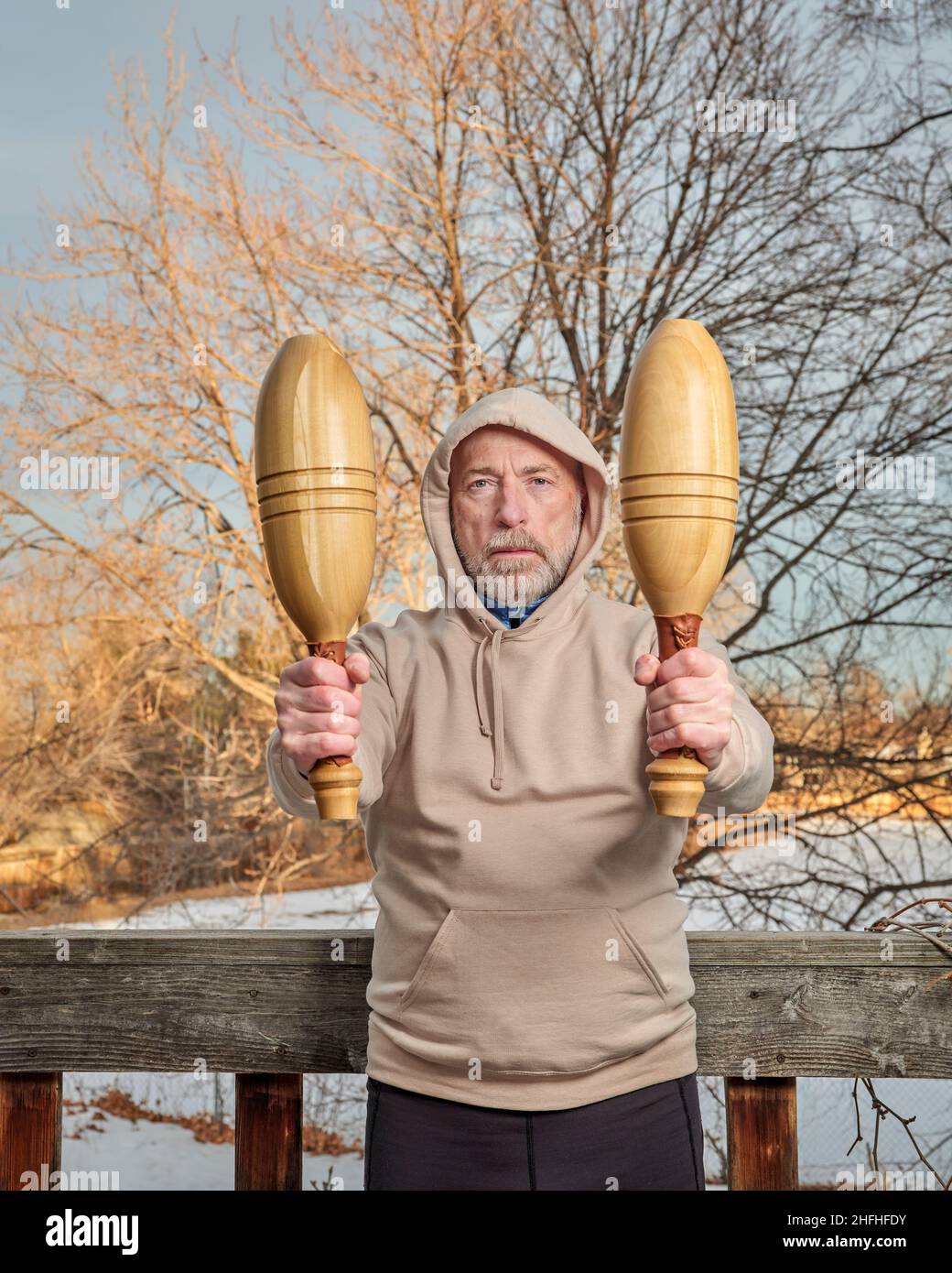 ritratto all'aperto di uomo anziano (alla fine del 60s) esercitandosi con i randelli indiani di legno nel suo cortile, pomeriggio di inverno, idoneità oltre 60 concetto Foto Stock