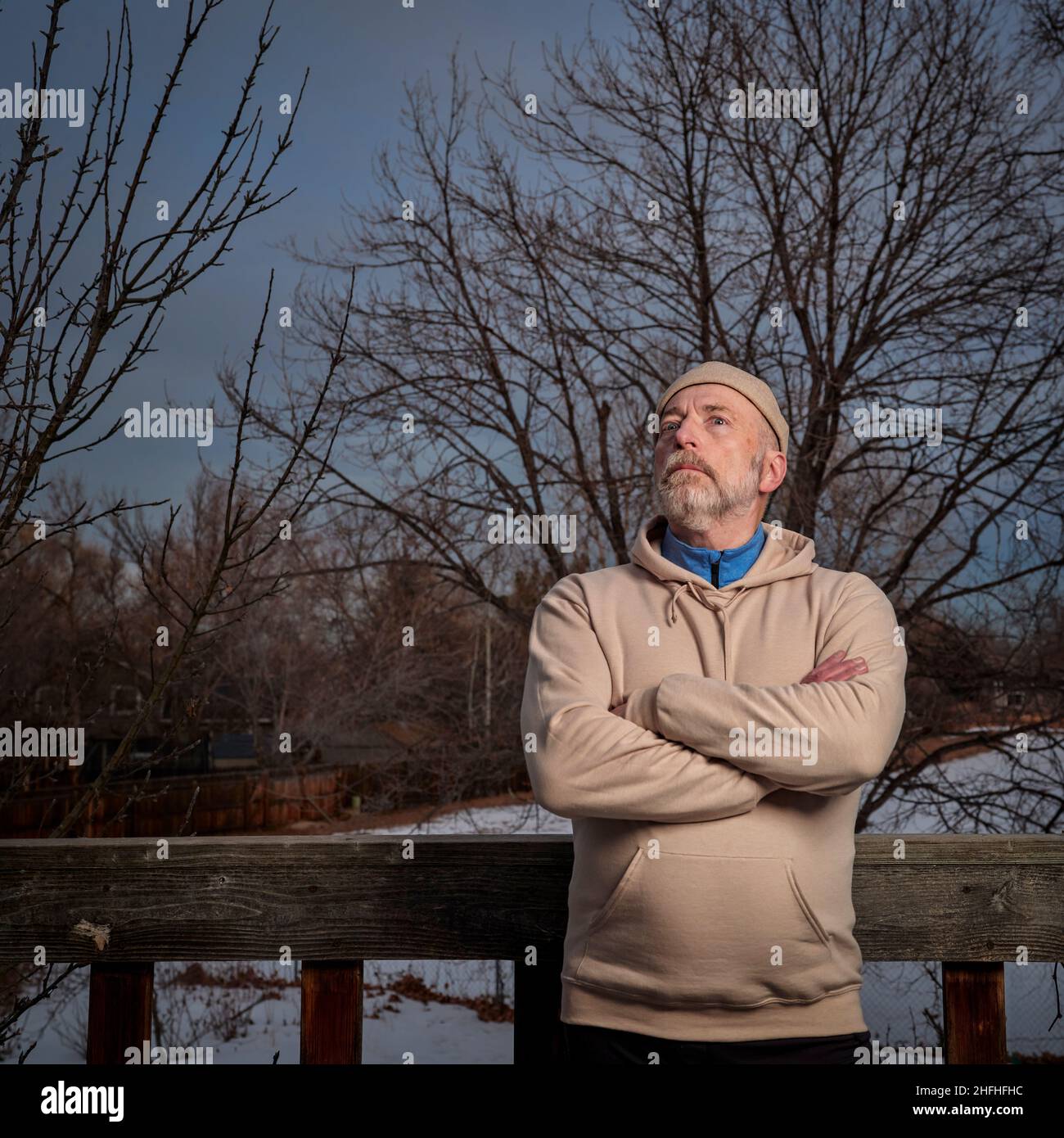 ritratto all'aperto di un uomo anziano in una felpa che si starreda al cielo notturno d'inverno nel suo cortile Foto Stock