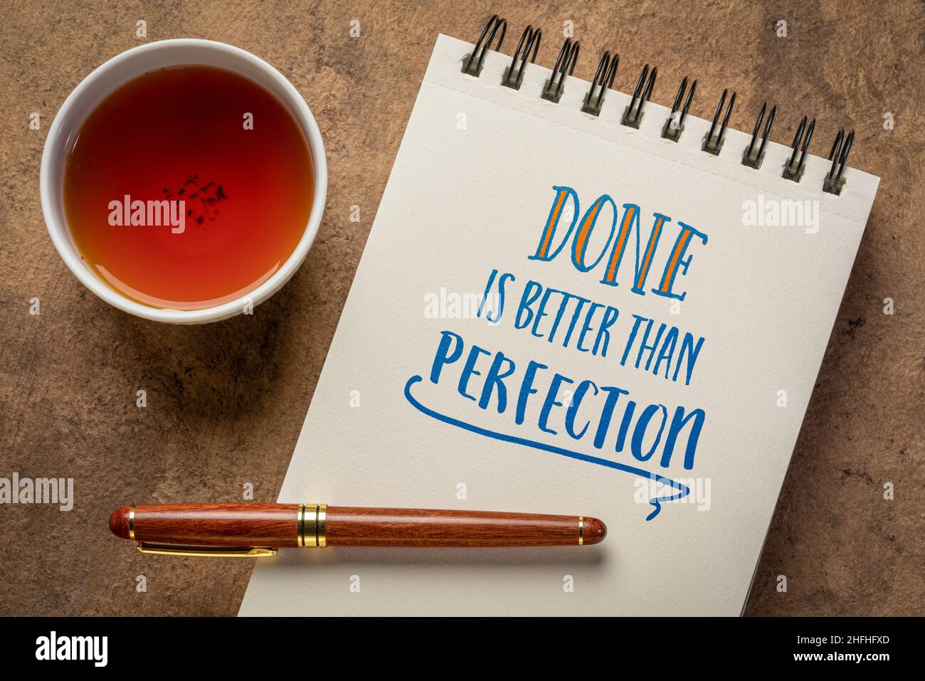 Fare è meglio di ricordare perfezione - scrittura a mano in un notebook a spirale con una tazza di tè, business, efficienza e concetto di produttività Foto Stock