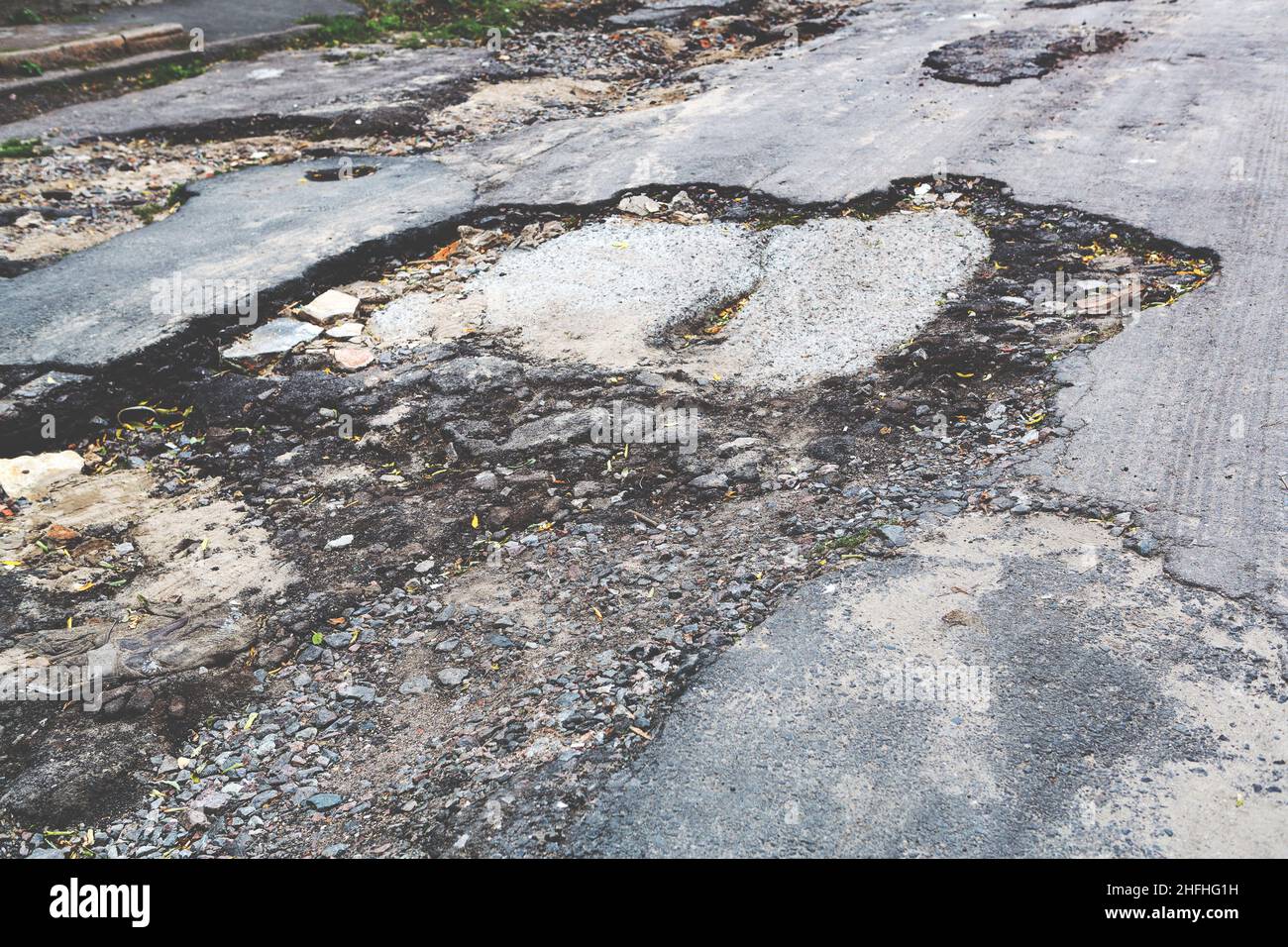 Una strada danneggiata da pioggia e neve, che necessita di manutenzione. Pavimentazione asfaltata rotta con conseguente buche, pericolosa per i veicoli. Foto Stock