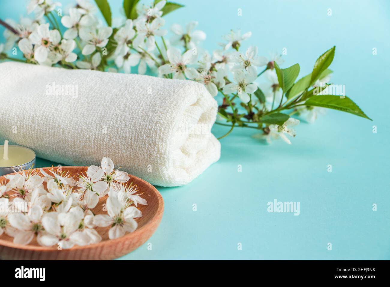 Concetto di benessere aromaterapico. Accessori per il benessere e il relax su sfondo blu. Olio aromatico, asciugamano, candela e fiori. Prodotto organico per la cura della pelle Foto Stock