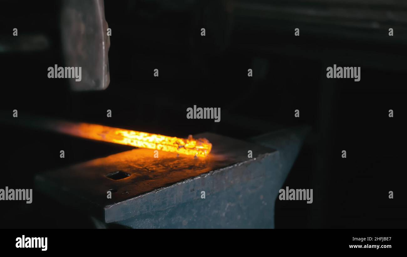 Forge workshop. Fucina di produzione manuale. Mani di Smith con il colpo di martello sul metallo incandescente, sull'incudine, il processo della forgiatura. Foto Stock