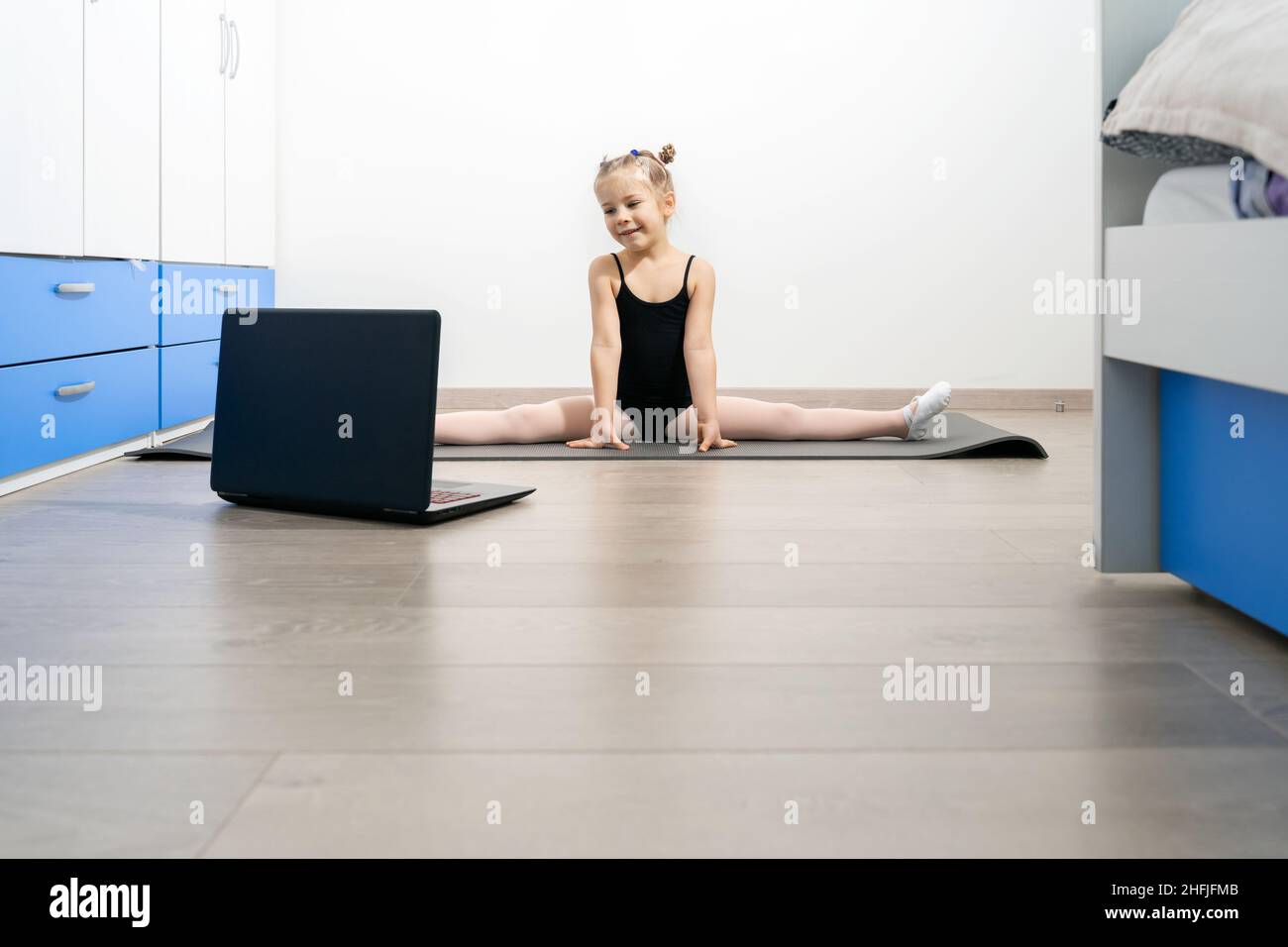 La ragazza piccola di ginnastica sta addestrando in linea con il laptop nel paese. Autoisolamento durante la quarantena. Foto Stock