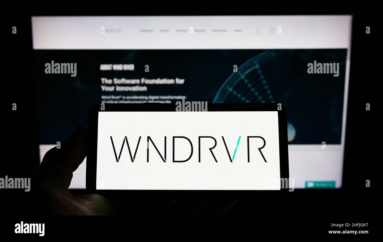 Persona che detiene il telefono cellulare con il logo della società americana di software Wind River Systems Inc. Sullo schermo di fronte alla pagina web. Mettere a fuoco sul display del telefono. Foto Stock