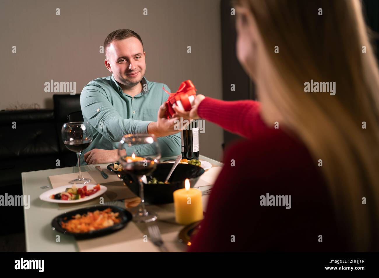 Due innamorati hanno cena a casa, una donna dà un uomo un regalo a sorpresa per un anniversario o San Valentino, festa di anniversario di matrimonio, romantico Foto Stock
