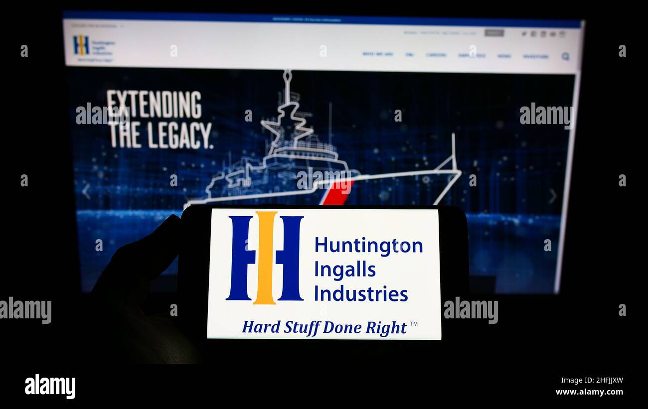 Persona che tiene uno smartphone con il logo della società statunitense Huntington Ingalls Industries Inc. (HII) sullo schermo di fronte al sito Web. Mettere a fuoco sul display del telefono. Foto Stock