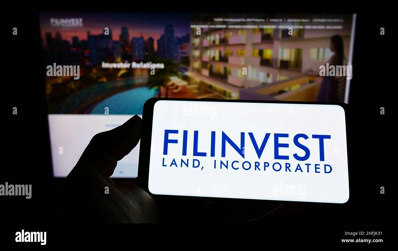 Persona che detiene il cellulare con il logo della società immobiliare Filinvest Land Inc. (FLI) sullo schermo di fronte al sito web aziendale. Mettere a fuoco sul display del telefono. Foto Stock