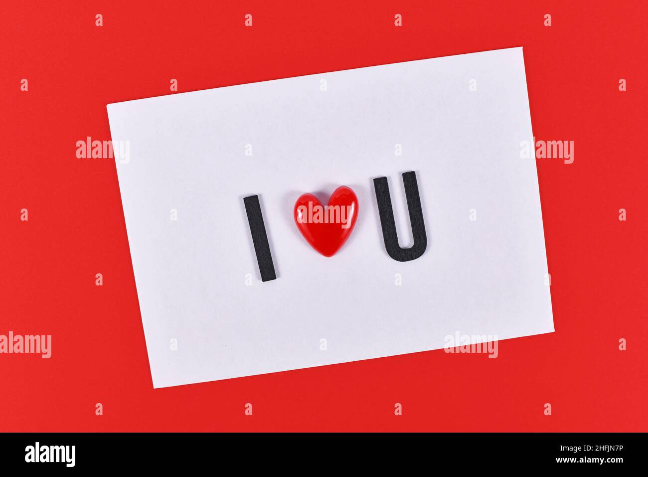 Il testo del giorno di San Valentino 'ti amo' è stato scritto con il cuore su carta bianca su sfondo rosso Foto Stock
