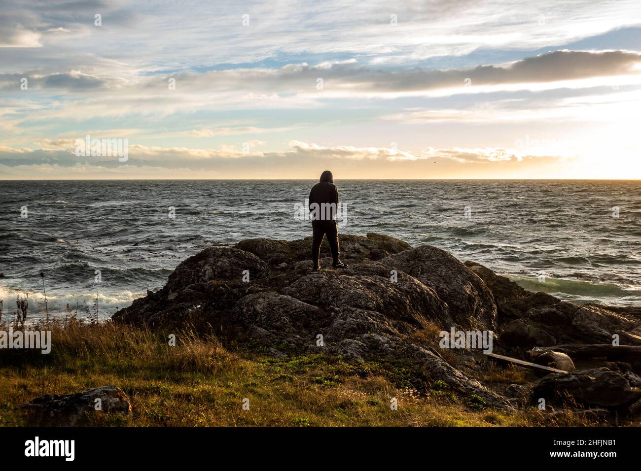 Vista di un uomo dalla silhouette che si erge sulla costa rocciosa dell'isola di San Juan al tramonto, con sottili nuvole bianche sullo sfondo Foto Stock