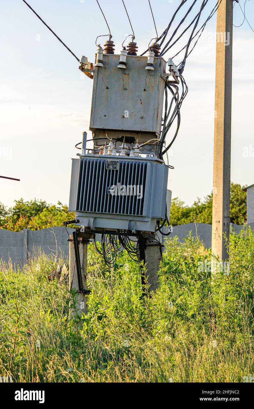 Trasformatore elettrico nel campo dietro il villaggio, fili e un palo. Apparecchiature elettriche di vecchio stile. Foto Stock