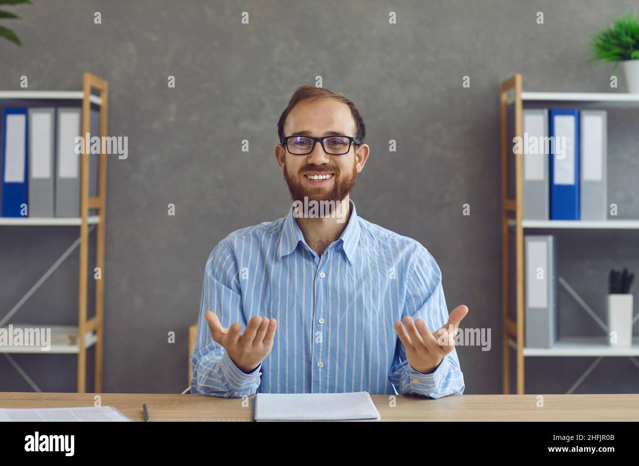 Uomo d'affari cordiale che parla con una videochiamata online mentre si siede in ufficio. Foto Stock