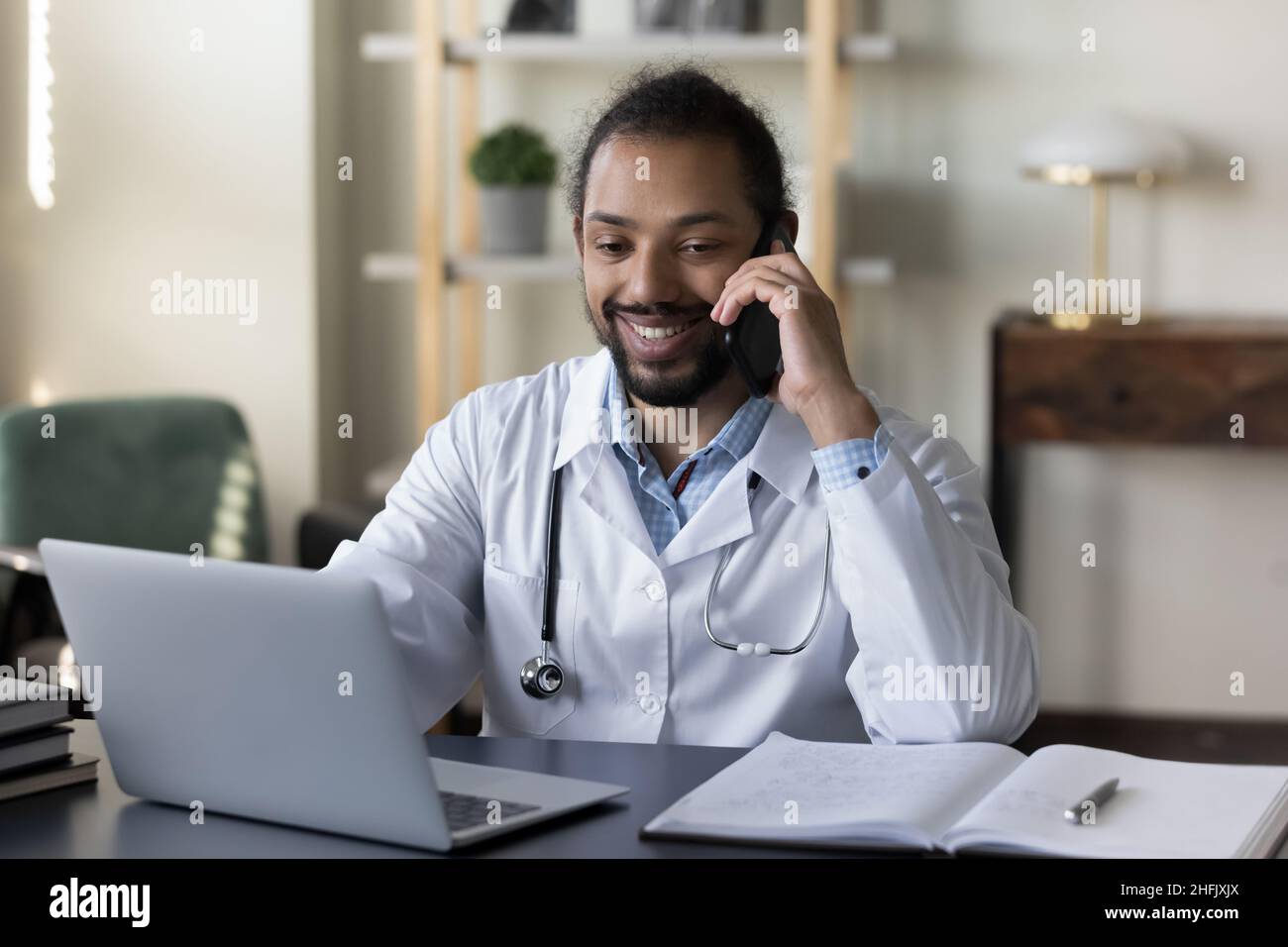 Sorridente giovane medico afroamericano maschile multitasking in ufficio. Foto Stock