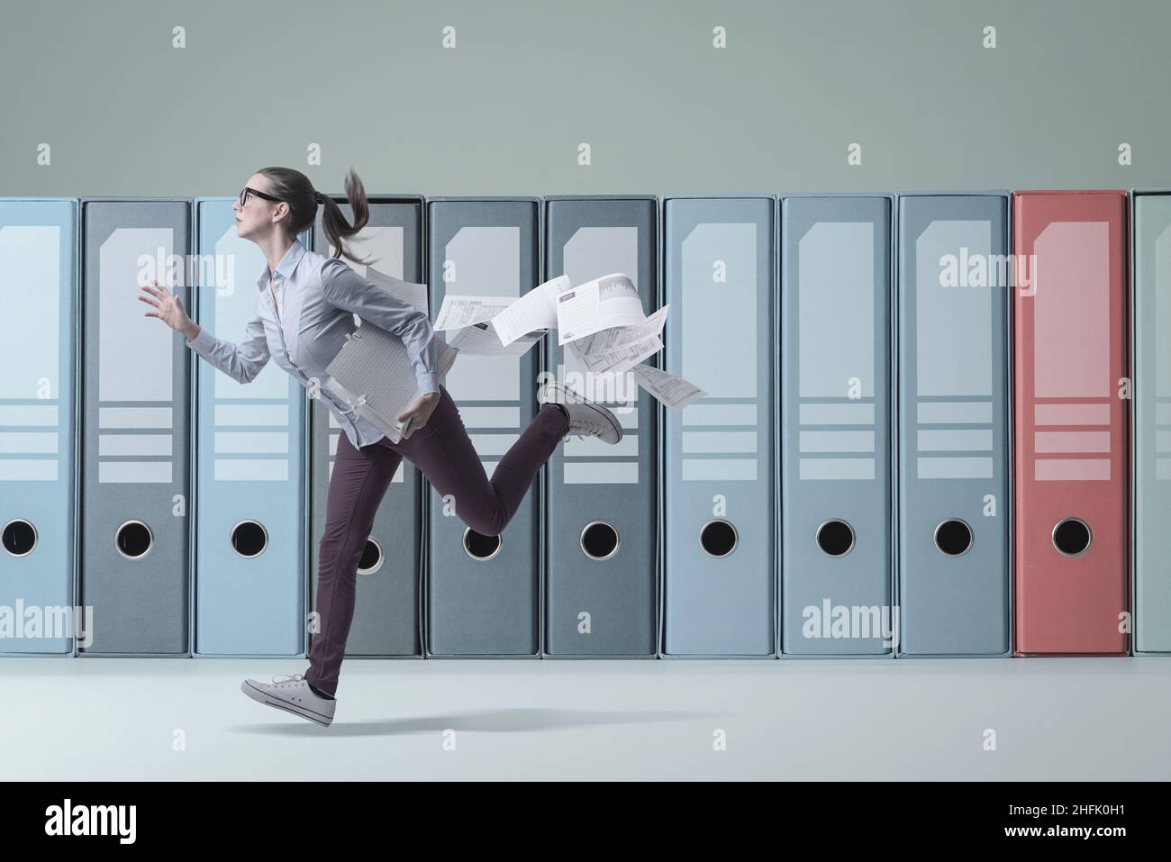 Distracted businesswoman che funziona e perde il suo lavoro di ufficio, scadenze e concetto di affari, raccoglitori enormi dell'anello nello sfondo Foto Stock