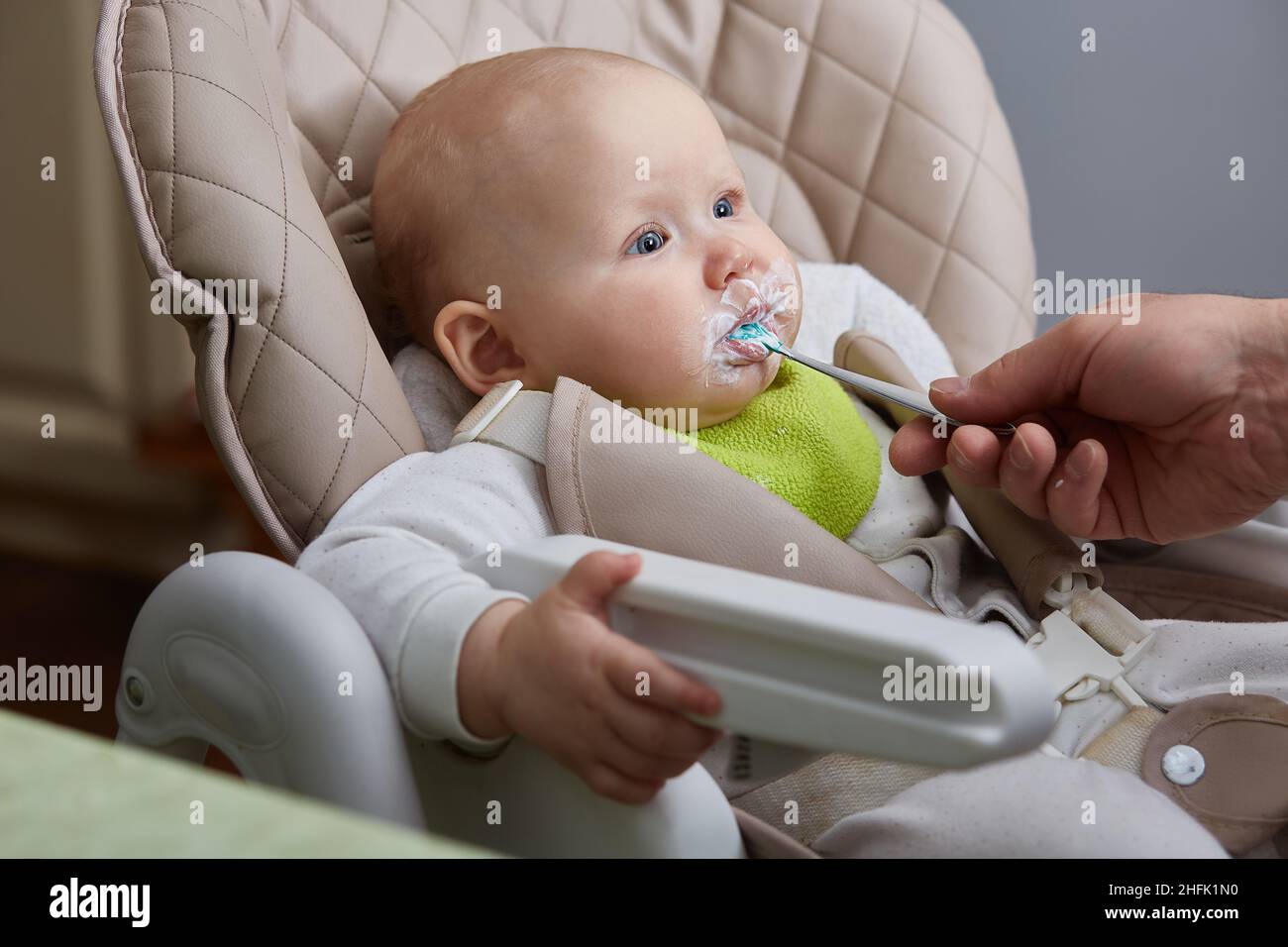 il bambino in una sedia del bambino mangia per la prima volta da un cucchiaio Foto Stock
