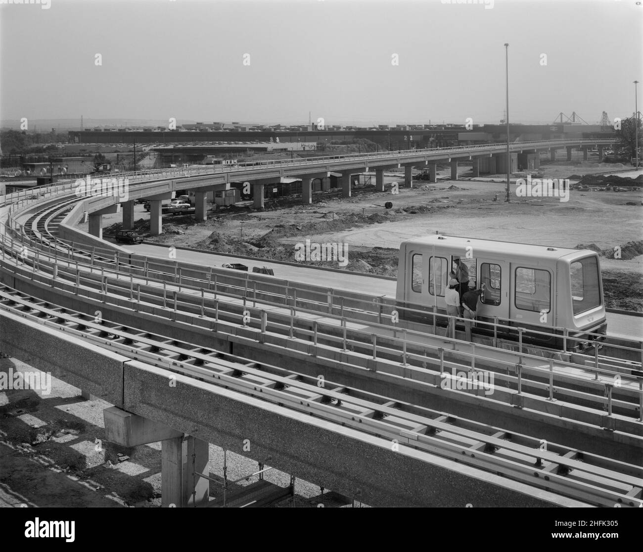 Aeroporto di Birmingham, Birmingham Maglev, Elmdon, Birmingham, Bickenhill, Solihull, 15/08/1983. I lavoratori ispezionano una nuova macchina Maglev sul nuovo sistema Maglev all'aeroporto di Birmingham, vicino alla fine della sua costruzione, con la stazione ferroviaria internazionale di Birmingham oltre. Il sistema Maglev all'aeroporto di Birmingham è stato il primo sistema Maglev commerciale al mondo. Ha usato la sospensione magnetica senza attrito per guidare le autovetture lungo una guida sopraelevata tra il terminal dell'aeroporto e la stazione ferroviaria internazionale di Birmingham. Sono state installate tre auto, ognuna delle quali poteva trasportare fino a 32 passeggeri e. Foto Stock