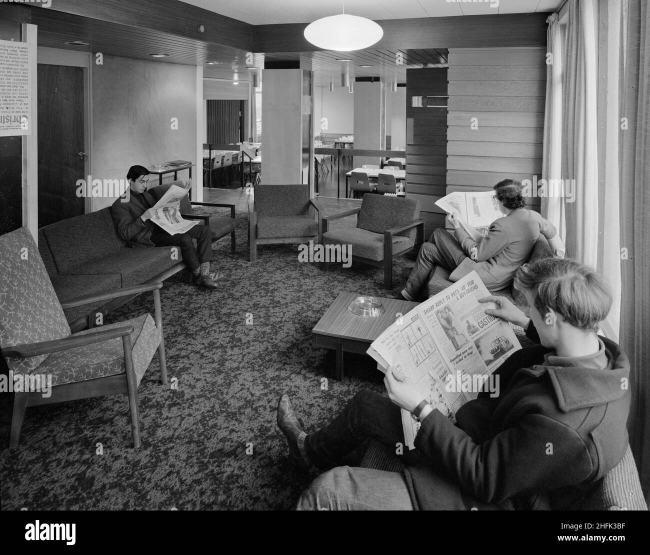 Parson's Field House, Durham University, Durham, County Durham, 08/12/1965. Tre uomini che leggono i giornali nella sala comune degli studenti nelle sale di residenza della casa di campo di Parson all'Università di Durham. Le sale di residenza del Parson's Field House sono state progettate dagli architetti Bernard Taylor e Associates e sono state costruite dalla Regione Settentrionale della Società di costruzione di Laing. Tre blocchi di quattro piani sono stati costruiti utilizzando laingwall prefabbricati in cemento, compreso il blocco uno che conteneva la sala da pranzo principale e sale comuni al piano terra con camere studio ai piani superiori, b Foto Stock