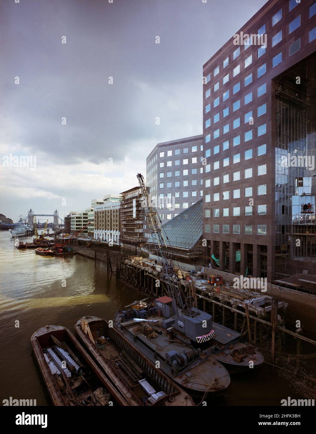 London Bridge City, Southwark, Greater London Authority, 01/04/1986. Guardando verso est lungo la riva sud del Tamigi verso il Tower Bridge, si vede il London Bridge City Complex sulla destra con chiatte in primo piano. Vari edifici all'interno di questo complesso di uffici, appartamenti e negozi su Tooley Street a London Bridge City sono stati costruiti da Laing Management Contracting per il gruppo St Martins che ha riprogettato l'ex sito di Hay's Wharf sulla riva sud del Tamigi. La riqualificazione del sito ha avuto luogo nel corso di 2 1/2 anni tra il 1985-1988 e includeva il London Bridge N.1, Cottons Foto Stock