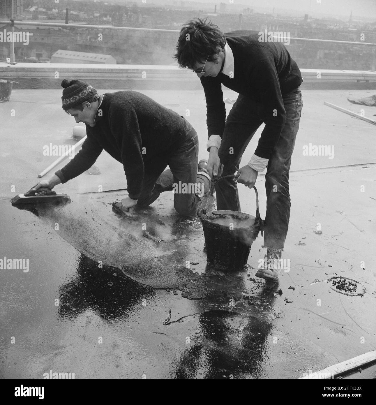 Doddington Estate, Battersea, Wandsworth, Londra, 08/04/1969. Due operai che asfaltano il tetto di un blocco di appartamenti durante la costruzione della tenuta di Doddington. Il Doddington Estate, appena fuori da Battersea Park Road, è stato progettato dagli architetti Emberton, Tardrew &amp; Partners. La tenuta, che comprendeva blocchi di appartamenti a torre, fu costruita tra il 1967-71 da Laing per il consiglio di Londra del Borough di Wandsworth. Fu costruito utilizzando il loro sistema di costruzione Jespersen del 12M, costituito da parti prefabbricate e pannelli prefabbricati in calcestruzzo prodotti nella loro fabbrica di calcestruzzo ad Andover. Foto Stock