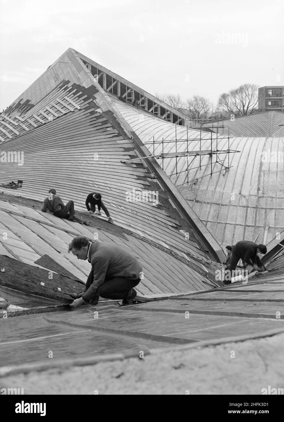 Commonwealth Institute, Kensington High Street, Kensington, Londra, 06/04/1962. Lavoratori che posano la pelle esterna di fogli di rame a prova di intemperie il tetto della sala espositiva presso il Commonwealth Institute. Laing costruì l'Istituto del Commonwealth tra l'ottobre 1960 e l'ottobre 1962 per sostituire l'ex Istituto Imperiale che doveva essere demolito per fare posto a nuove strutture presso l'Imperial College. L'edificio era costituito da un blocco amministrativo a quattro piani che conteneva una biblioteca, un ristorante, una sala riunioni e una sala conferenze e da un blocco separato a due piani contenente un cinema con una galleria d'arte sopra, Foto Stock
