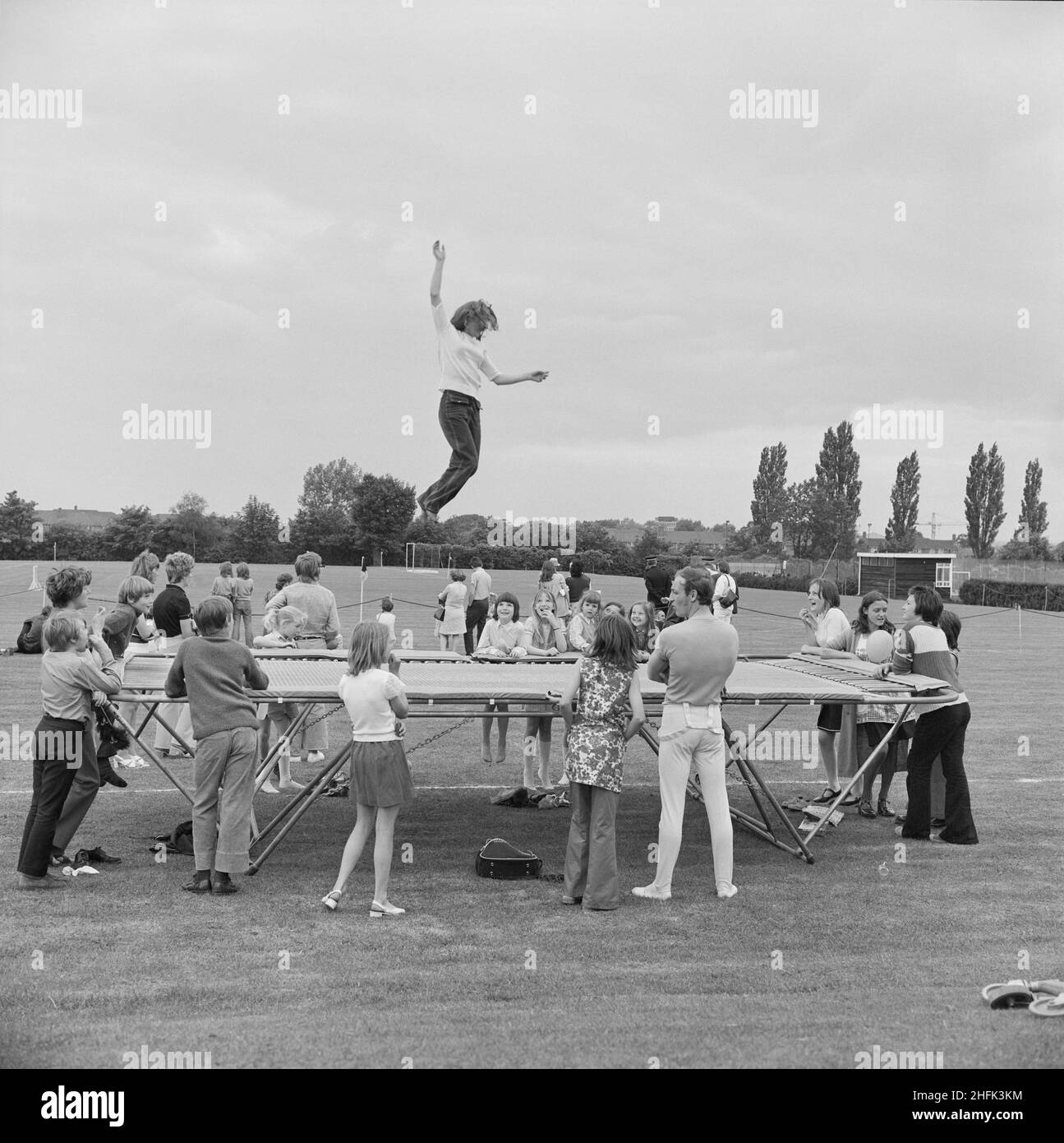 Laing Sports Ground, Rowley Lane, Elstree, Barnet, Londra, 09/06/1973. Un gruppo di persone si è riunito attorno, guardando una ragazza che salta su un trampolino durante l'annuale Gala Day che si tiene presso il Laing Sports Ground di Elstree. La Giornata annuale di Gala si è tenuta presso il Laing Sports Ground il 9th giugno 1973. Le attrazioni includono dimostrazioni di cani di polizia, velivoli modello, la Royal British Legion band, corse per bambini e sport. La sera c'erano balli e bingo nella Club House, e "birra e picchiata" nel tendone. Oltre 2.000 persone hanno partecipato al gala, e più di 600 persone hanno soggiornato per l'intrattenimento serale Foto Stock