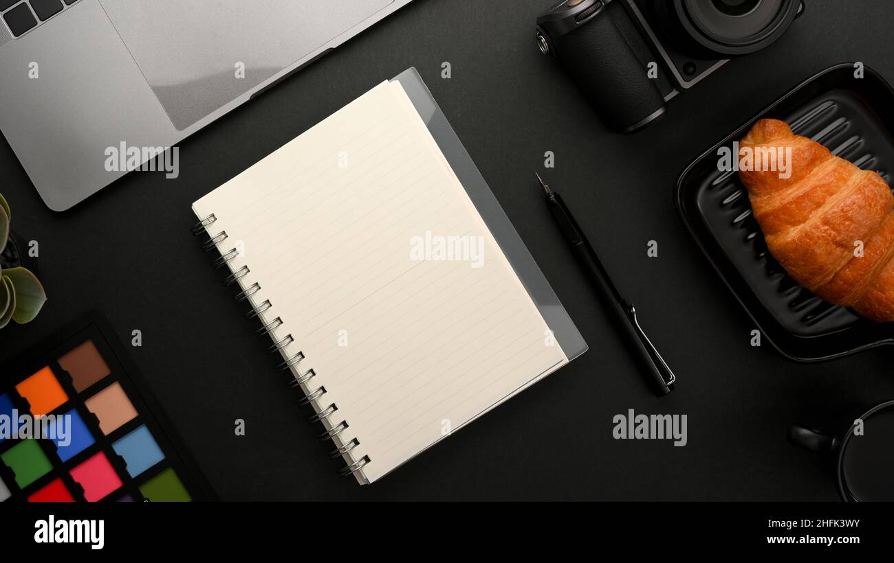 Area di lavoro moderna per fotografi o grafici con notebook e strumenti di lavoro su sfondo nero. Foto Stock
