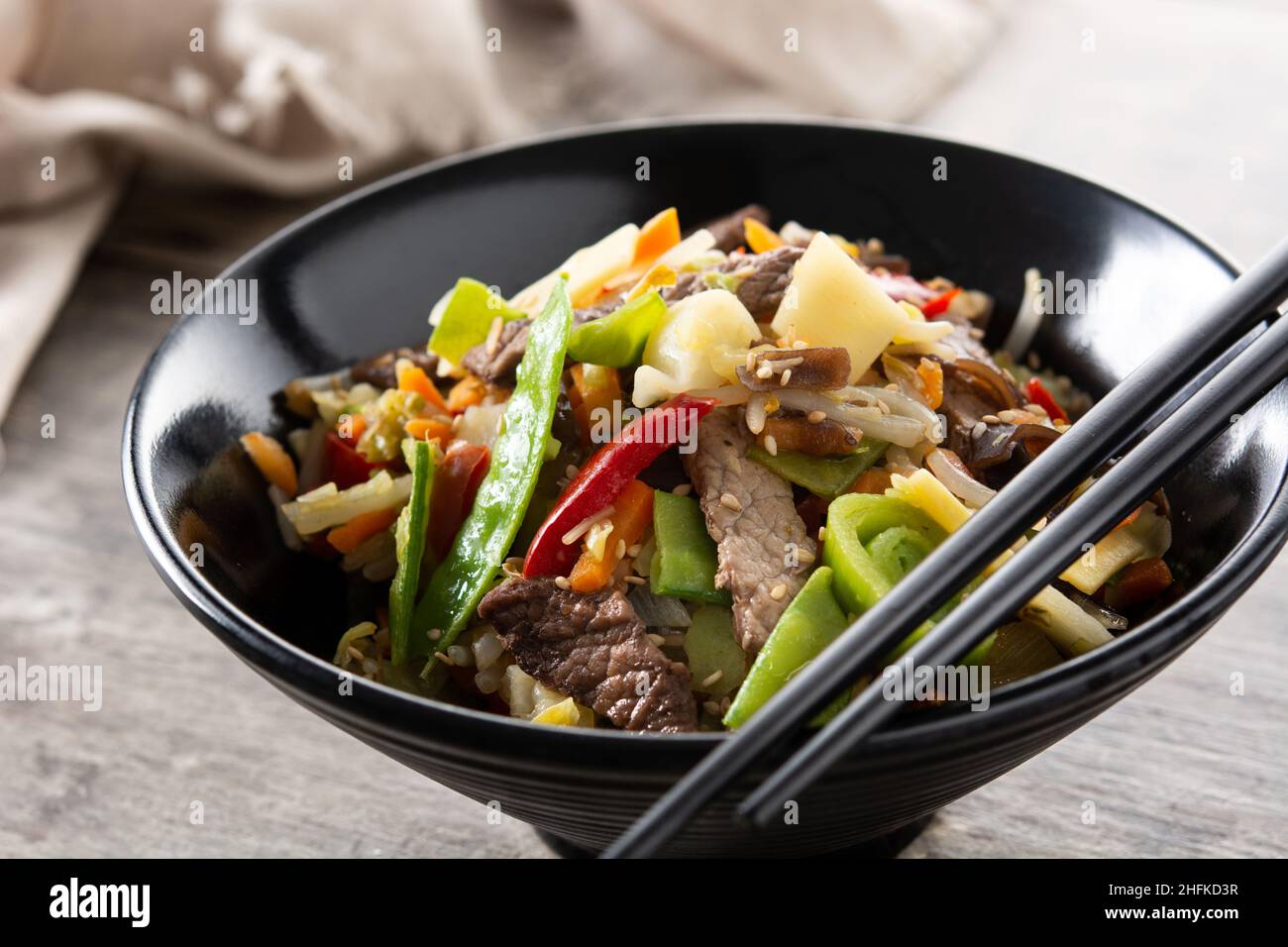 Manzo, verdure e semi di sesamo in una ciotola nera su un tavolo di legno Foto Stock