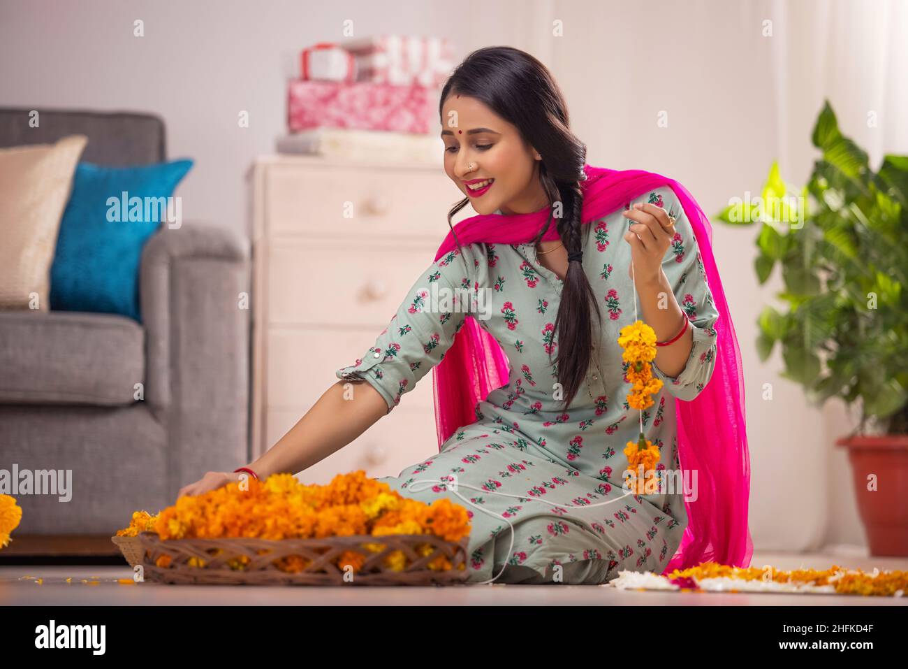 Donna indiana da sola che fa una tradizionale ghirlanda di fiori marigold Foto Stock