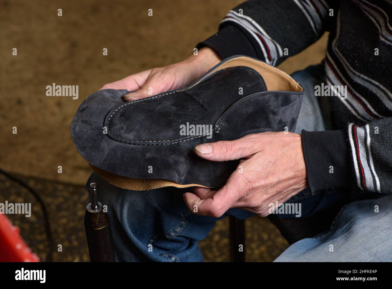 Bootmaker fare scarpe seduti in officina. Calzolaio che tiene in mano la scarpa scamosciata grigia prima della cucitura. Scarpe fatte a mano su misura Foto Stock